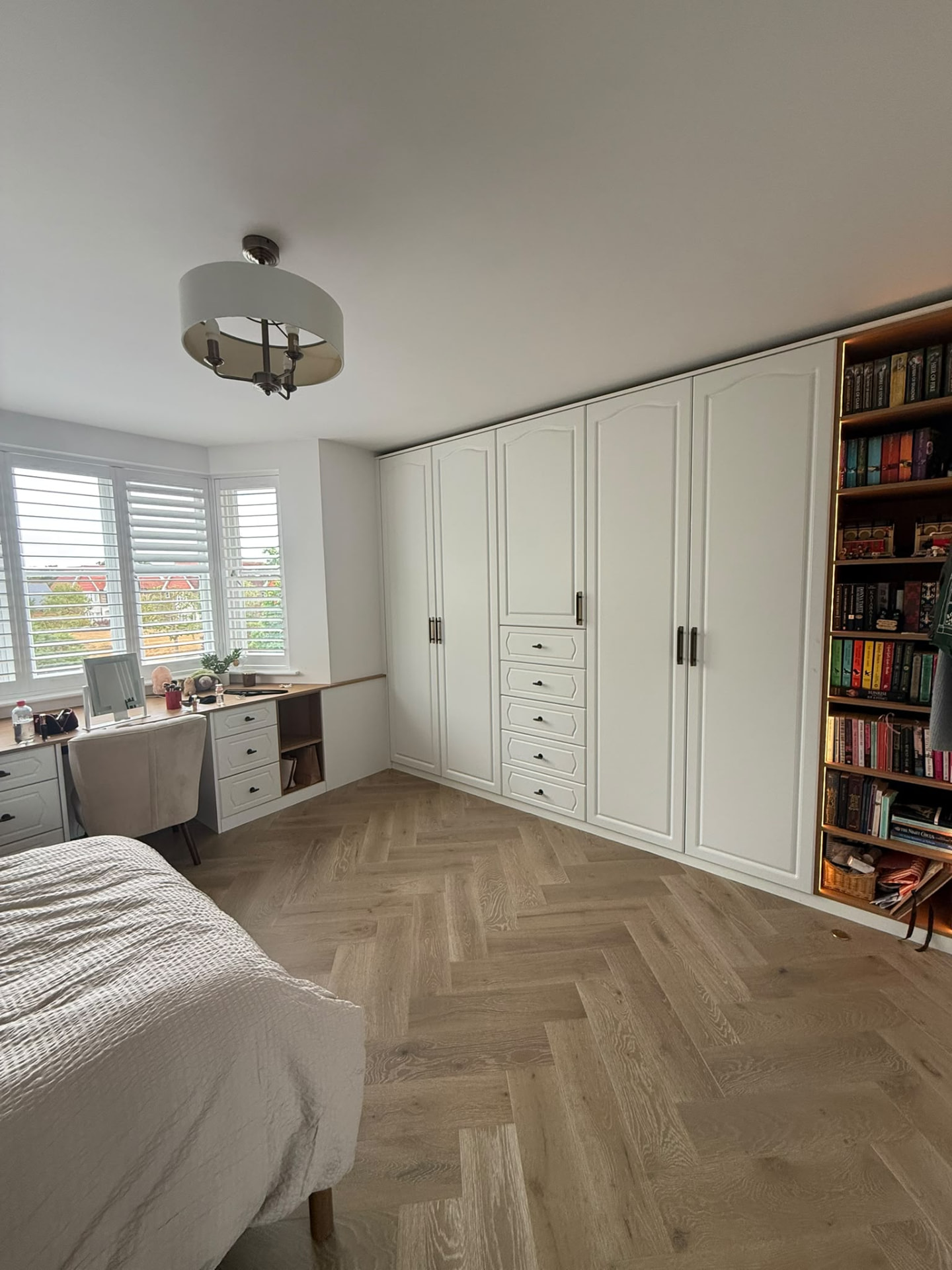 White fitted wardrobes with central drawer stack beside a bay-window dressing table