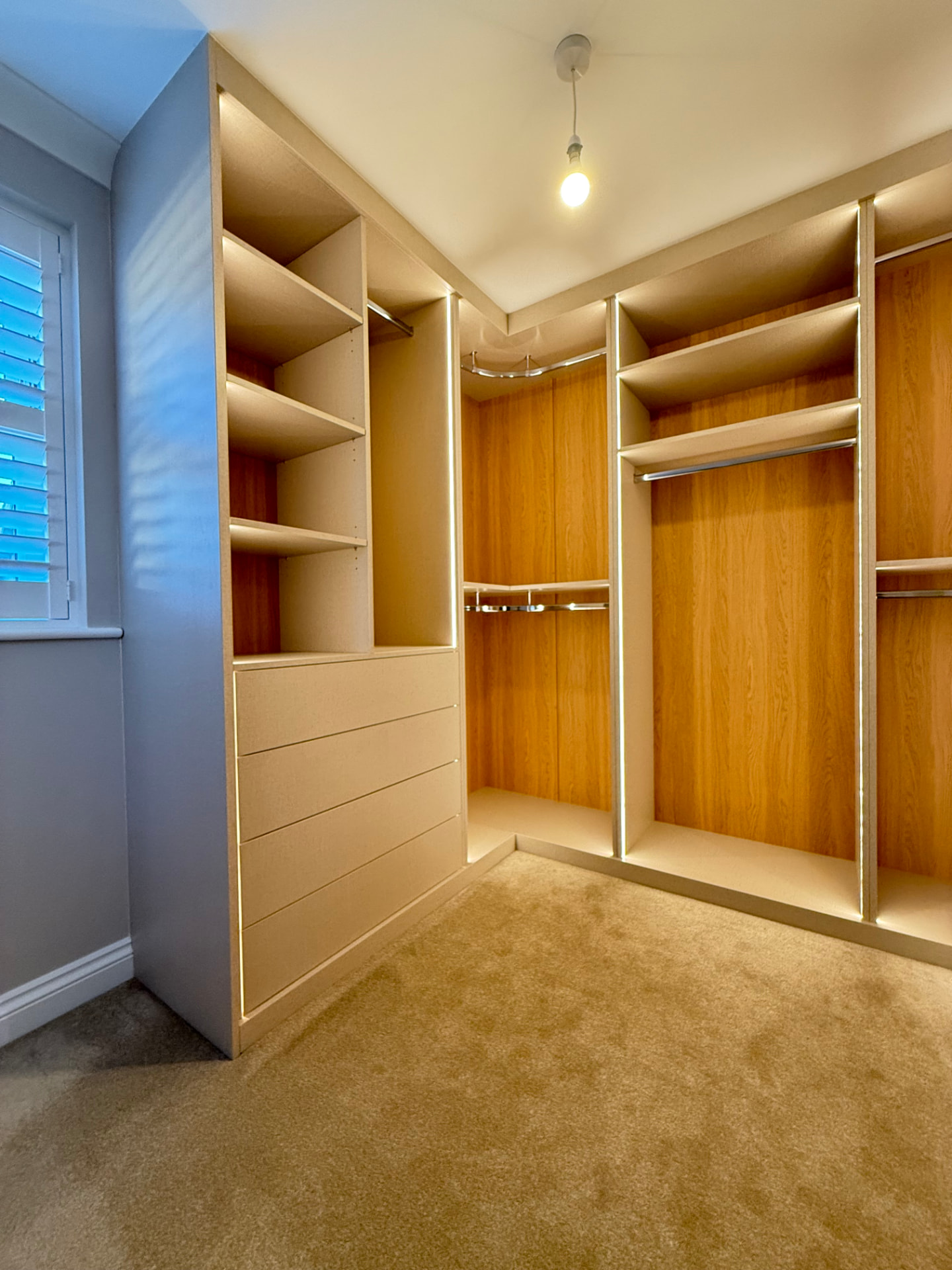 Bespoke walk-in wardrobe with hanging rails, drawer stacks and warm LED strip lighting