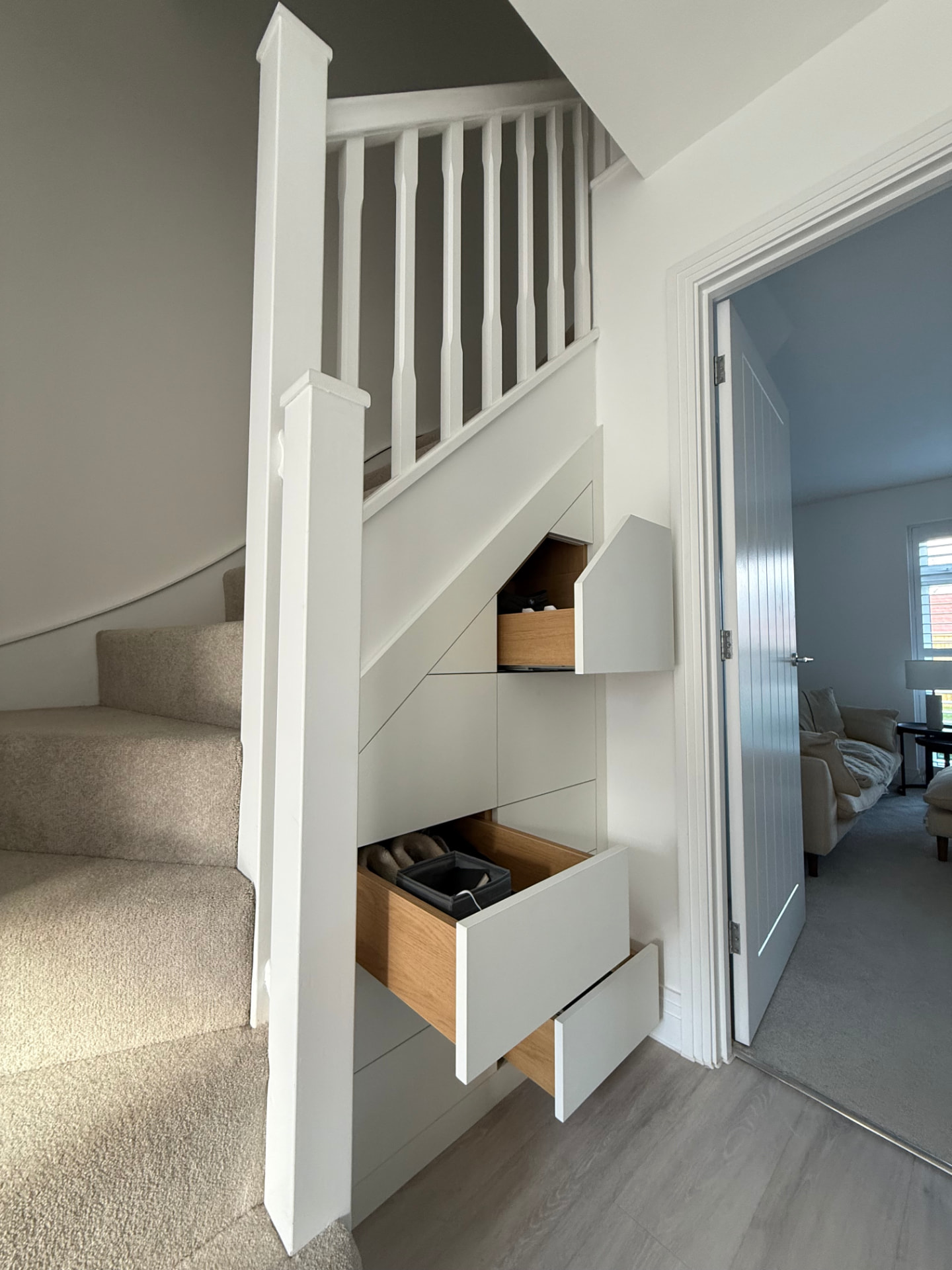 Under-stairs fitted drawers and cupboards in pale grey with oak-lined interiors