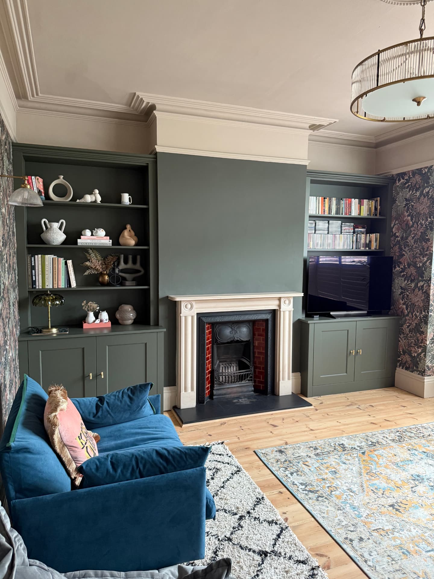 Dark green fitted alcove cabinets and shelving flanking a period fireplace
