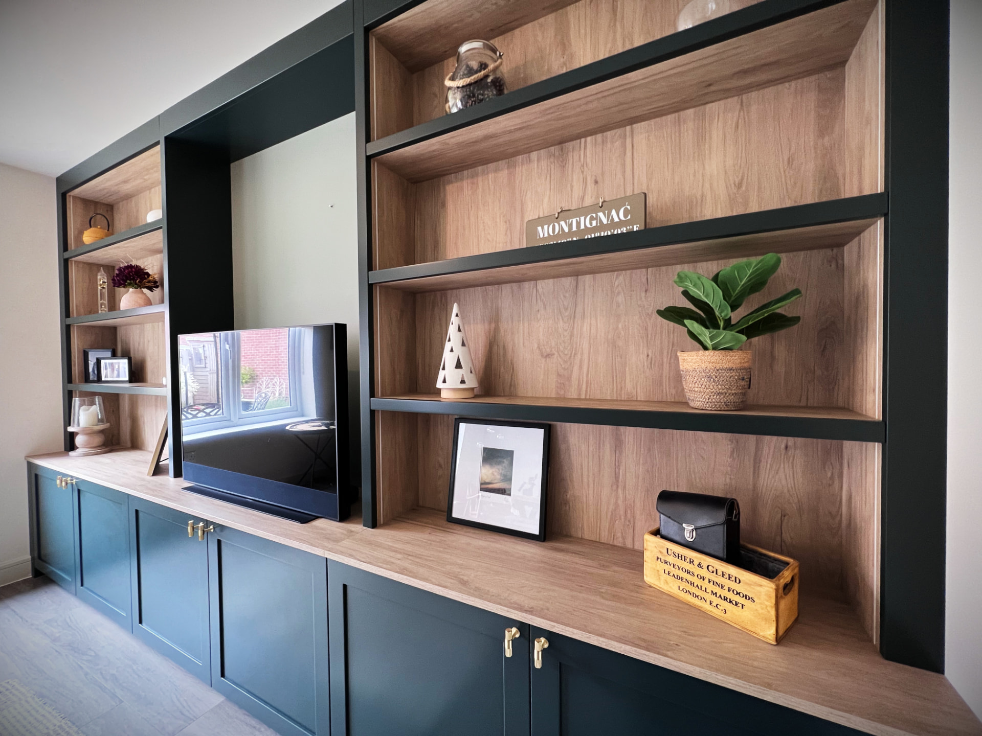 Dark green framed media wall with oak-backed shelving, base cabinets and brass handles